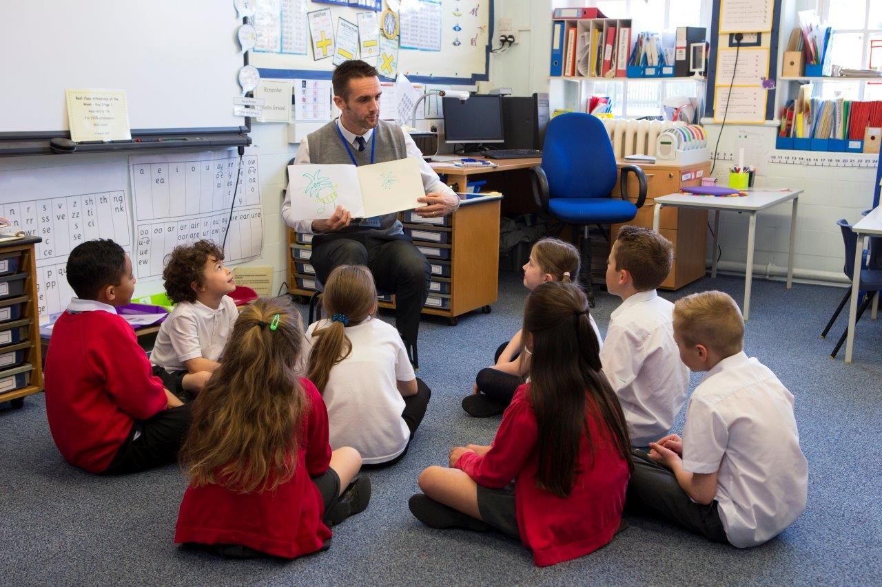 male teacher reading to primary pupils